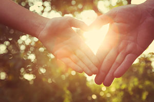 Two people are touching fingers and forming a heart in the sunlight
