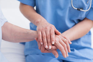 A female Nurse is comforting an elderly male patient by holding his hand
